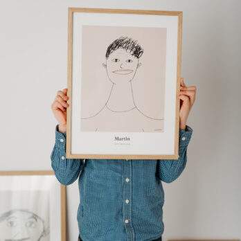 Dijete drži uokvireni poster napravljen od vlastitog crteža, prikazan u neutralnoj monokromatskoj boji.