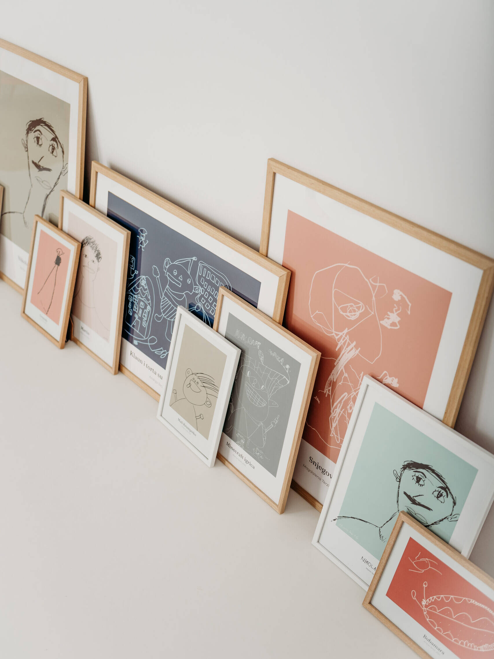 Personalizirani posteri izrađeni od dječjih crteža u različitim bojama i veličinama, uokvireni i naslonjeni na zid.